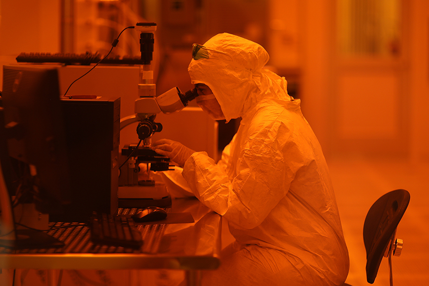 Researcher in clean room looking through a microscope
