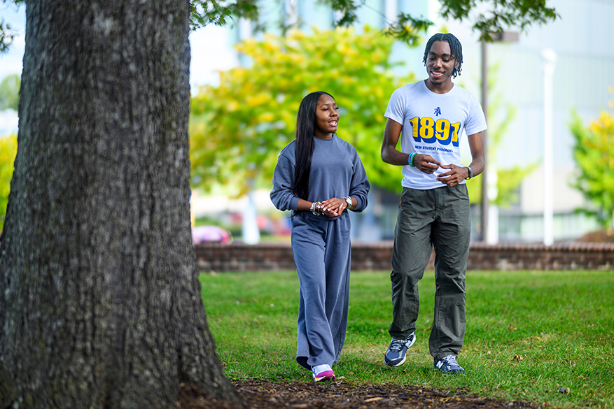 Young woman and man talking on campus on the grass near a tree