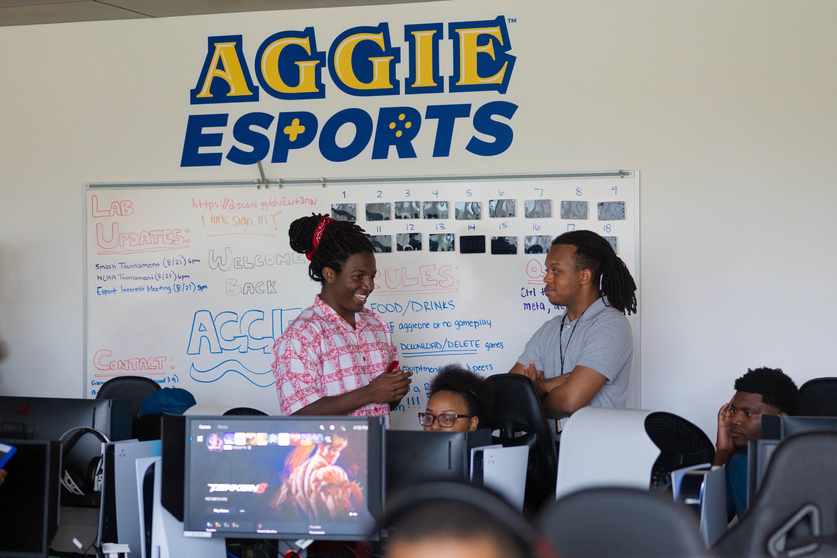 Happy student under the Aggie Esports sign in the lab